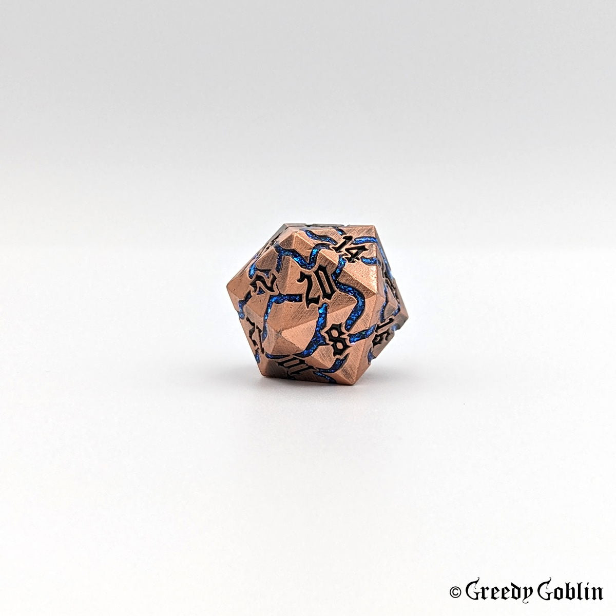 A metal D20 die that has a copper color and blue mica veins. The numbers are black and the die is displayed on a white background.