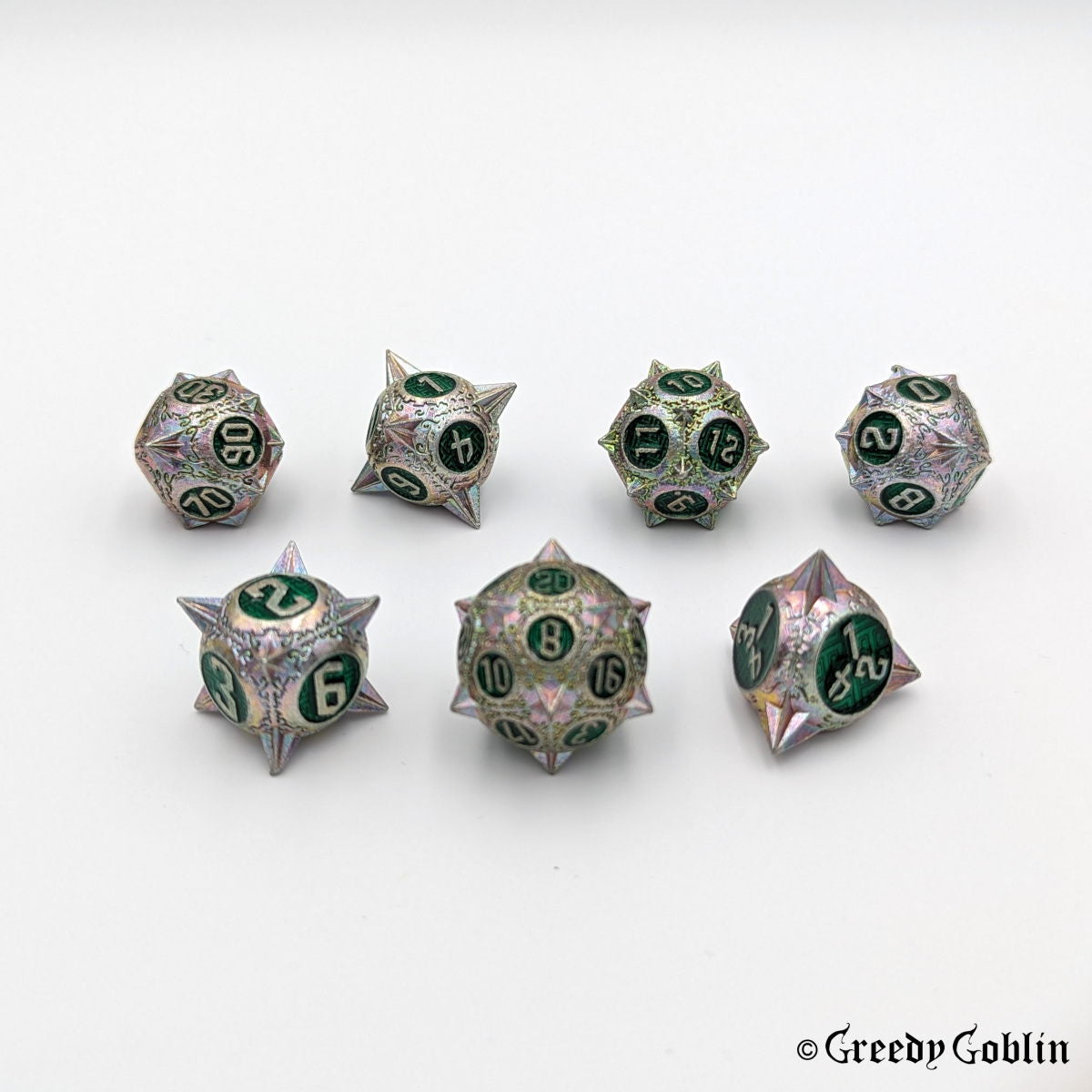 Metal DnD dice set (D4, D6, D8, D12, D20, 2x D10) with sharp edges and oil-slick finish. The engravings behind the numbers are dark green.