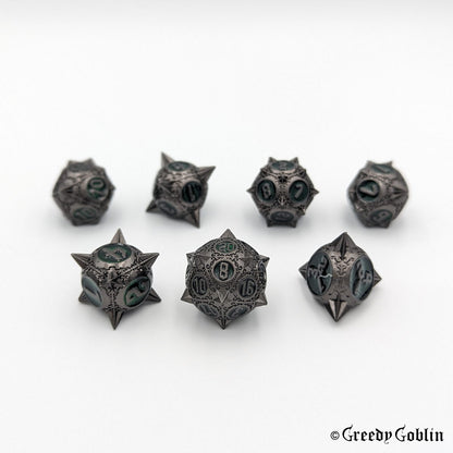 Metal DnD dice set (D4, D6, D8, D12, D20, 2x D10) with sharp edges and gunmetal finish. The engravings behind the numbers are dark green.