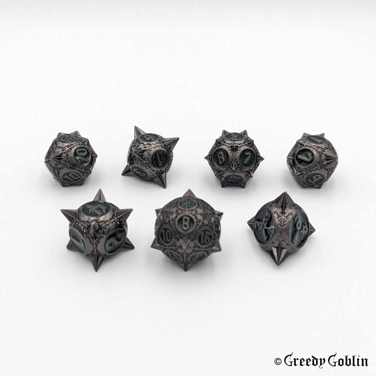 Metal DnD dice set (D4, D6, D8, D12, D20, 2x D10) with sharp edges and gunmetal finish. The engravings behind the numbers are dark green.