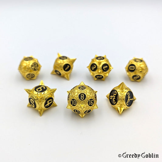 Metal DnD dice set (D4, D6, D8, D12, D20, 2x D10) with sharp edges and gold finish. The engravings behind the numbers are black.