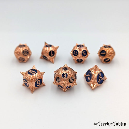 Metal DnD dice set (D4, D6, D8, D12, D20, 2x D10) with sharp edges and copper finish. The engravings behind the numbers are deep blue.
