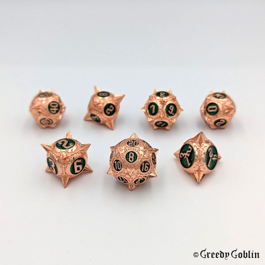 Metal DnD dice set (D4, D6, D8, D12, D20, 2x D10) with sharp edges and copper finish. The engravings behind the numbers are deep green.
