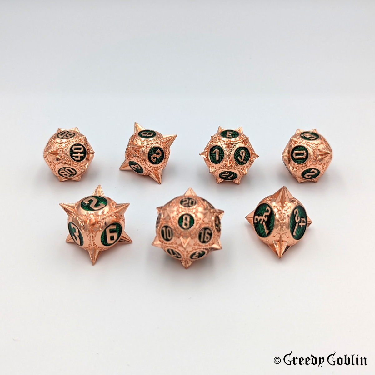 Metal DnD dice set (D4, D6, D8, D12, D20, 2x D10) with sharp edges and copper finish. The engravings behind the numbers are deep green.