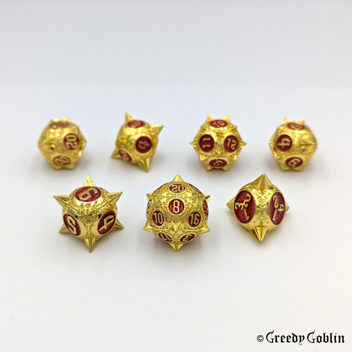 Metal DnD dice set (D4, D6, D8, D12, D20, 2x D10) with sharp edges and gold finish. The engravings behind the numbers are red.