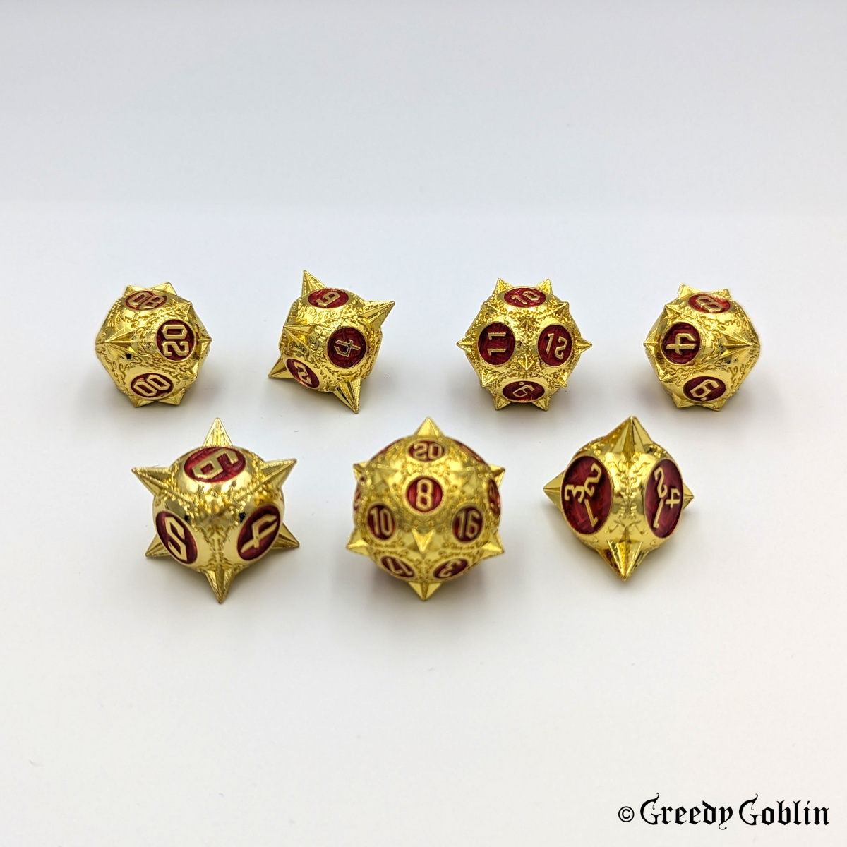 Metal DnD dice set (D4, D6, D8, D12, D20, 2x D10) with sharp edges and gold finish. The engravings behind the numbers are red.